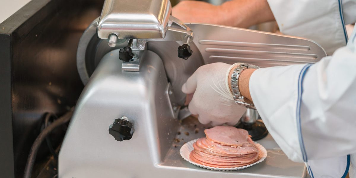 chef wearing rubber glove  using ham slicer machine